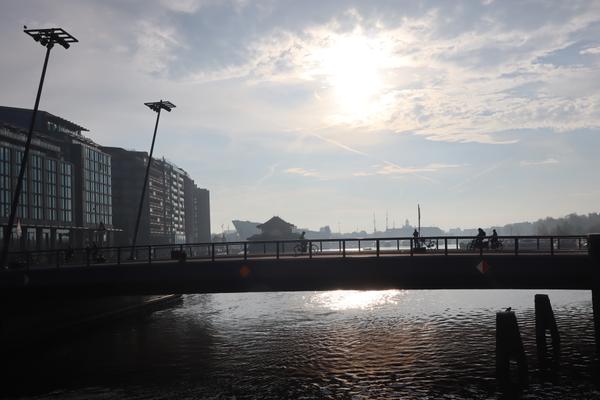 The photo captures a bright morning scene over a city canal, with a bridge spanning the water